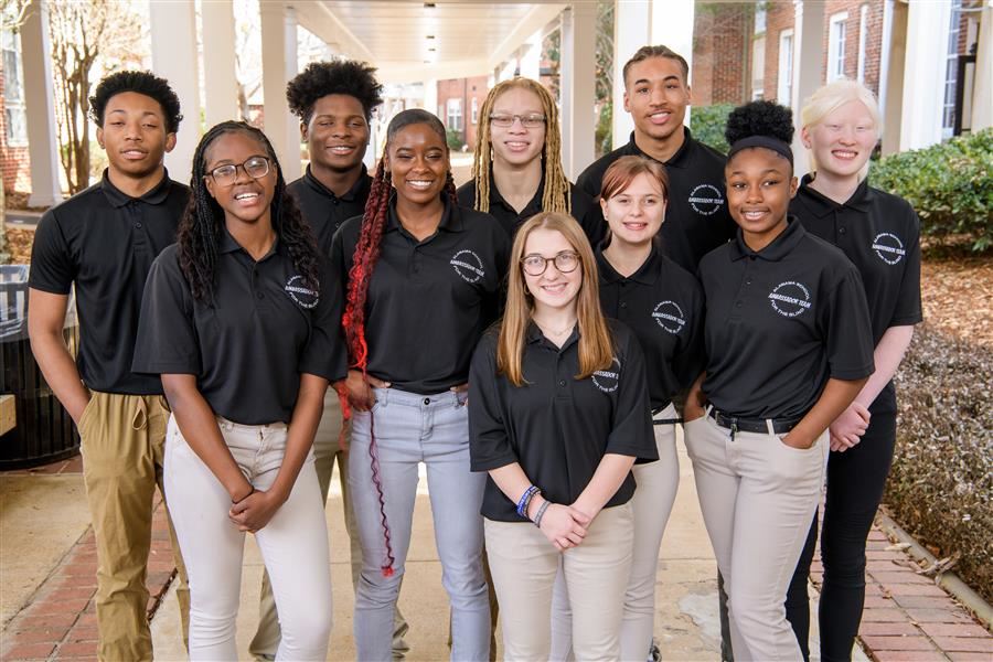  Ten students wearing black polos and khaki pants smile to the camera. 